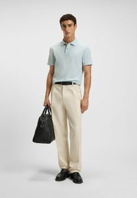 Light blue polo shirt, beige trousers, black belt, black bag with handle, and black shoes; smooth fabric and tailored design.