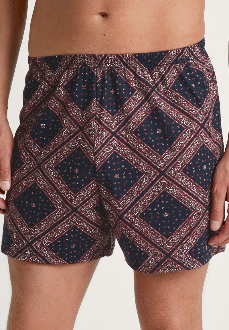 Marineblauwe zwemshorts met een rood-wit paisley diamantpatroon, elastische tailleband en een loose-fit ontwerp. Zachte stoftextuur.
