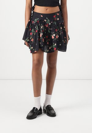 Mini-jupe noire à fleurs avec des détails froncés, portée avec des chaussettes blanches et des mocassins noirs, associée à un top court noir.
