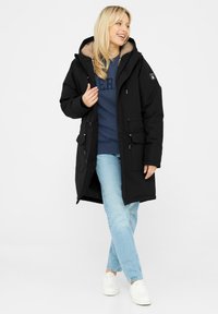 Černá parka s kožichovou kapucí, zapínání na zip a knoflíky, dvě přední kapsy a nastavitelná šňůrka v pase a na spodním lemu.