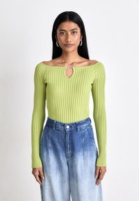 Maglietta a maniche lunghe a coste di colore verde chiaro con scollatura a chiave, abbinata a pantaloni in denim blu con ombre a vita alta.