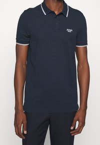 Marinblå polo shirt i bomull med klassisk krage, treknappslå och vita ränder på kragen och ärmarna.