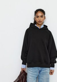 Černá oversized mikina s kapucí na stažení, dlouhými raglánovými rukávy, žebrovanými manžetami a mírně texturovaným povrchem, doplněná světlými džíny.