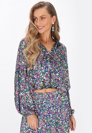 Bunt gemusterte Bluse und passender Rock mit einem lebhaften Blumenmuster. Der Stoff wirkt leicht, mit einer lockeren Passform und langen Ärmeln.