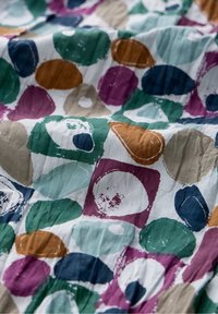 Multicolor stof met cirkelvormige en ovale vormen in groen, paars, blauw, oranje en beige op een witte achtergrond. Zichtbare kreukeltextuur.