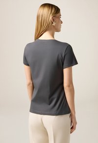 Camiseta gris de manga corta con un cuello redondo, textura suave y dobladillo recto, combinada con pantalones de color claro.
