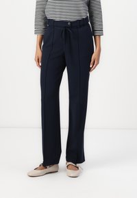 Pantalones navy con cinturón en la cintura, con cierre de botón, dos costuras delanteras y ajuste relajado. Combinados con bailarinas de color beige claro.
