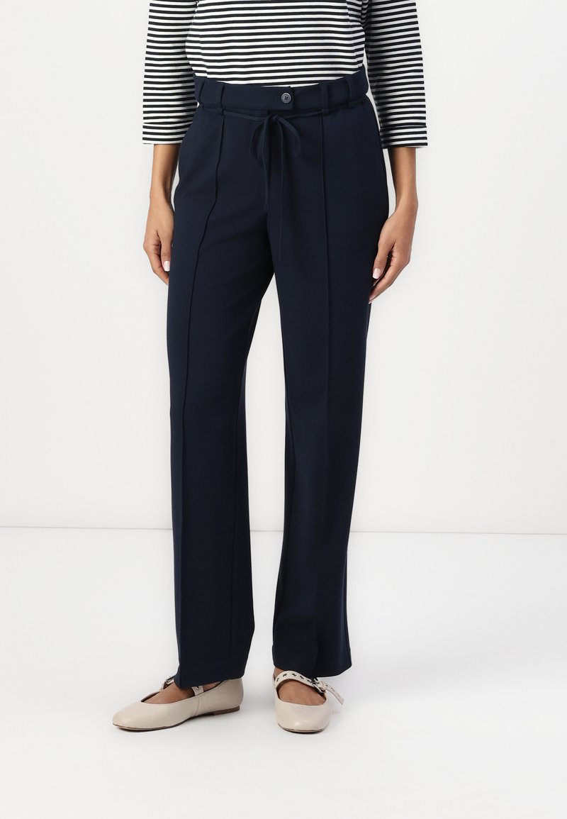 Pantalones navy con cinturón en la cintura, con cierre de botón, dos costuras delanteras y ajuste relajado. Combinados con bailarinas de color beige claro.