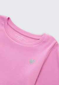 Maglietta rosa a coste con scollatura rotonda, caratterizzata da un piccolo ricamo a forma di cuore in argento sulla parte anteriore. Il materiale sembra morbido e leggero.