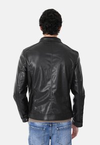 Giubbotto di pelle nera con un design aderente, texture liscia e colletto classico, abbinato a jeans in denim azzurro chiaro.