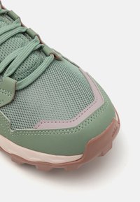 Lichtgroene sportschoen met een bovenwerk van mesh, rubberen buitenzool en textuuraccenten in roze en bruin. Vetersluiting met een gevoerd kraagje.