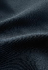 Dunkelblauer Stoff mit einer strukturierten, gewebten Oberfläche, die sanfte Falten und einen subtilen Glanz zeigt. Nahaufnahme, die die Materialdetails hervorhebt.