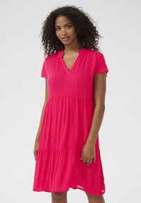 Short-sleeved, V-neck dress in bright pink fabric; features a tiered design with a flowing silhouette and textured surface.