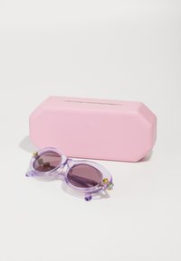 Ochelari de soare violeți, semi-transparenți, cu lentile ovale, accente aurii și un etui texturat roz în spatele lor, evidențiind un design elegant și modern.