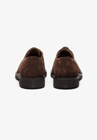 Brune semsko med en glatt tekstur, avrundet form og svart gummisåle. Har et minimalistisk design uten synlige detaljer.