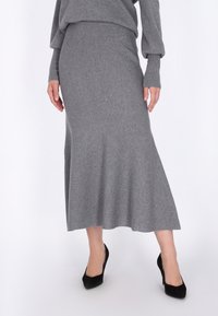 Jupe midi en tricot gris avec un ourlet évasé, texture lisse et taille ajustée. Associée à des chaussures à talons hauts noires.