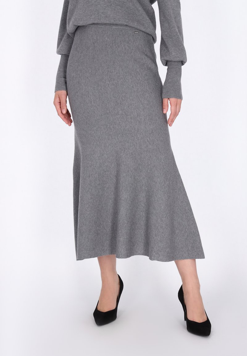 Jupe midi en tricot gris avec un ourlet évasé, texture lisse et taille ajustée. Associée à des chaussures à talons hauts noires.