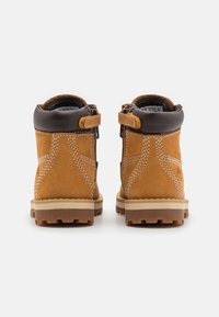 Braune Wildleder-Stiefel mit einem braunen Lederkragen und weißen Nähten. Verfügt über einen seitlichen Reißverschluss und eine robuste, strukturierte Laufsohle.