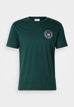 Dark green cotton t-shirt with a crew neckline and short sleeves. Features a circular logo in red, white, and blue on the chest.