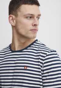 Striped cotton t-shirt featuring horizontal navy and white stripes, a crew neckline, and a small embroidered orange logo on the chest.