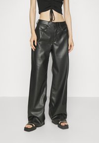 Hoge taille zwarte leren wijde broek met een gladde textuur, knoopsluiting en riemlussen. Draagt met een cropped top en sandalen.