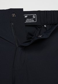 Czarne spodnie o gładkiej fakturze, z zamkiem i zapięciem na guzik, elastycznym pasem oraz metką wskazującą rozmiar S i regularny krój.