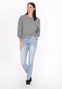 Fekete-fehér csíkos pulóver laza szabással, világoskék skinny farmernadrággal és fekete tornacipővel párosítva. Sima textúrájú, hétköznapi dizájn.