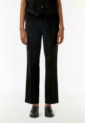 Schwarze Wildleder-Hosen im geraden Schnitt mit glatter Textur, kombiniert mit schwarzen Leder-Schlupfschuhen. Verfügt über ein minimalistisches Design ohne Muster.