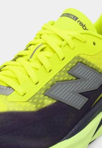 Αθλητικό παπούτσι νέον κίτρινο με γκρι λεπτομέρειες, που διαθέτει υφασμένο πάνω μέρος, ανθεκτικά κορδόνια και λευκό λογότυπο στο πλάι.