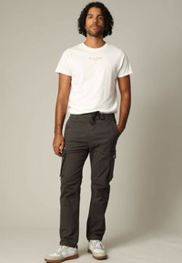 Witte T-shirt met korte mouwen en kleine tekst, gecombineerd met donkere cargobroek met zijzakken en een trekkoord. Gemaakt met witte sneakers.