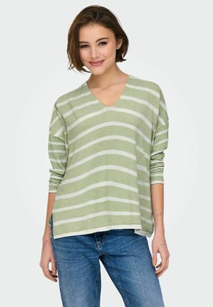 Suéter verde a rayas con escote en V y rayas horizontales blancas, de manga larga, corte relajado y dobladillo trasero ligeramente más largo. Combinado con jeans azules.