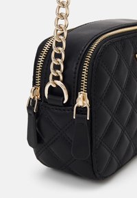 Sort quiltet håndtaske med guld hardware, kædderem og dobbelt lynlås. Materialet er struktureret syntetisk læder med en fast form.