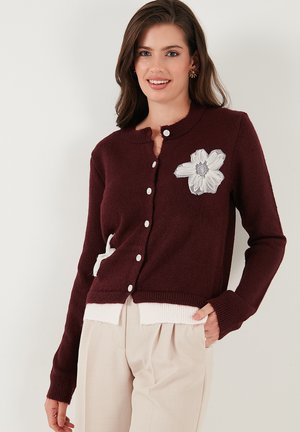 Burgundy cardigan with a round neckline, white flower embroidery, and button closures. Knit material with ribbed cuffs and hem.
