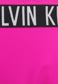 Roza tkanina s glatkom teksturom koja ima crni pojas s natpisom "CALVIN KLEIN" velikim, kontrastnim bijelim slovima.
