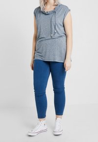 Šedý top s krátkým rukávem a lodičkovým výstřihem, kombinovaný s modrými skinny džíny a bílými vysokými teniskami. Jednoduchý, ležérní design.