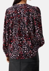 Blusa a maniche lunghe in tessuto nero con un motivo astratto rosa e rosso; presenta un collo rotondo e dettaglio arricciato sulle spalle.