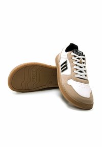 Zapatillas blancas y beige con parte superior de ante y cuero, detalles en negro y suela de goma texturizada que presenta la palabra "FREE".