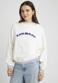 Sweat-shirt blanc avec broderie "SATURDAY SOCIAL CLUB" en rose et bleu. Présente des poignets et un ourlet côtelés avec des rayures bleu marine. Coupe décontractée.