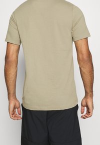 Camiseta de manga corta y cuello redondo en color caqui claro, hecha de algodón suave, con una textura lisa y un dobladillo recto.