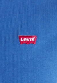 T-shirt bleu avec une texture côtelée présentant un logo Levi's rouge, brodé sur le devant, centré et avec un contour blanc.