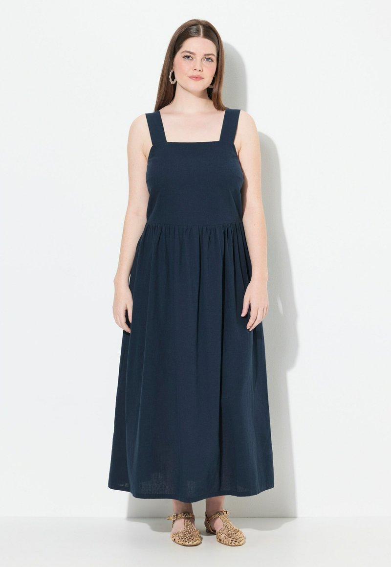 Sinih merenjang maxi dress dengan leher persegi, tali tebal, garis pinggang berkerut, dan rok mengalir. Ditampilkan pada seorang model yang mengenakan sandal anyaman.