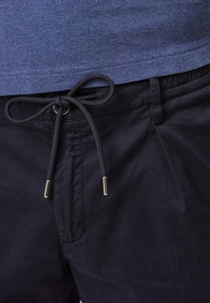 Top azul texturizado sobre pantalones negros de cintura elástica con cordón. El cordón tiene extremos de metal. Vista en primer plano de la ropa.
