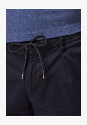 Blauwe textuurtop boven zwarte elastische broek met een koord. Het koord heeft metalen uiteinden. Close-up van de kleding.