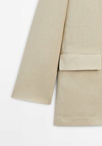 Manche de blazer en lin beige avec une poche pliée, une texture lisse et une couture simple, avec une forme légèrement structurée.