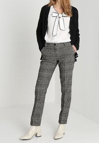 Czarno-białe, w kratę dopasowane spodnie o wysokim stanie, w połączeniu z białą bluzką z kokardą i czarnym kardiganem.