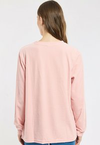 Chemise à manches longues en tissu côtelé rose pâle. Dotée d'un col rond et d'une coupe décontractée, avec des manches à poignets et un ourlet légèrement arrondi.