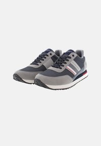 Sneaker grigi e blu navy realizzati in materiali mesh e scamosciati, con lacci tondi, un accento a strisce e una suola bianca e rossa.