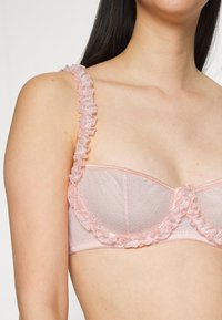 Sutiã de renda rosa claro com alças em babados e um padrão texturizado, apresentando um design clássico com suporte de aro.