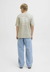 Lichtgrijs katoenen T-shirt met een bloemgrafiek en de tekst "ESSENTIALS DEPT." op de achterkant, gecombineerd met baggy blauwe denim jeans.
