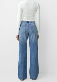 Vaqueros de pierna ancha en azul claro, confeccionados en denim, con cintura alta, grandes bolsillos traseros y un acabado ligeramente desgastado.